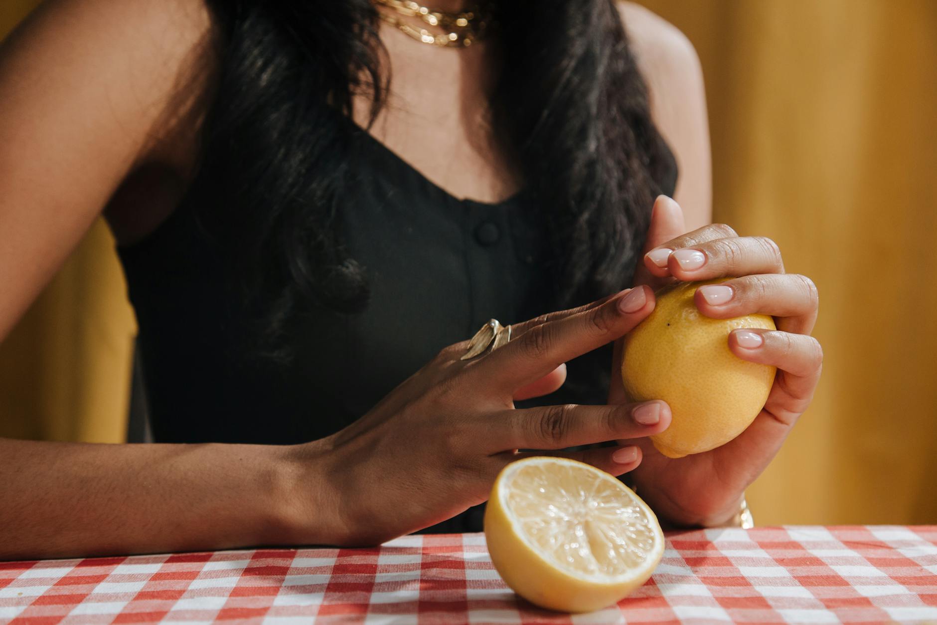 A hand with white nails holding a fresh lemon on a soft pink background surrounded by additional lemons