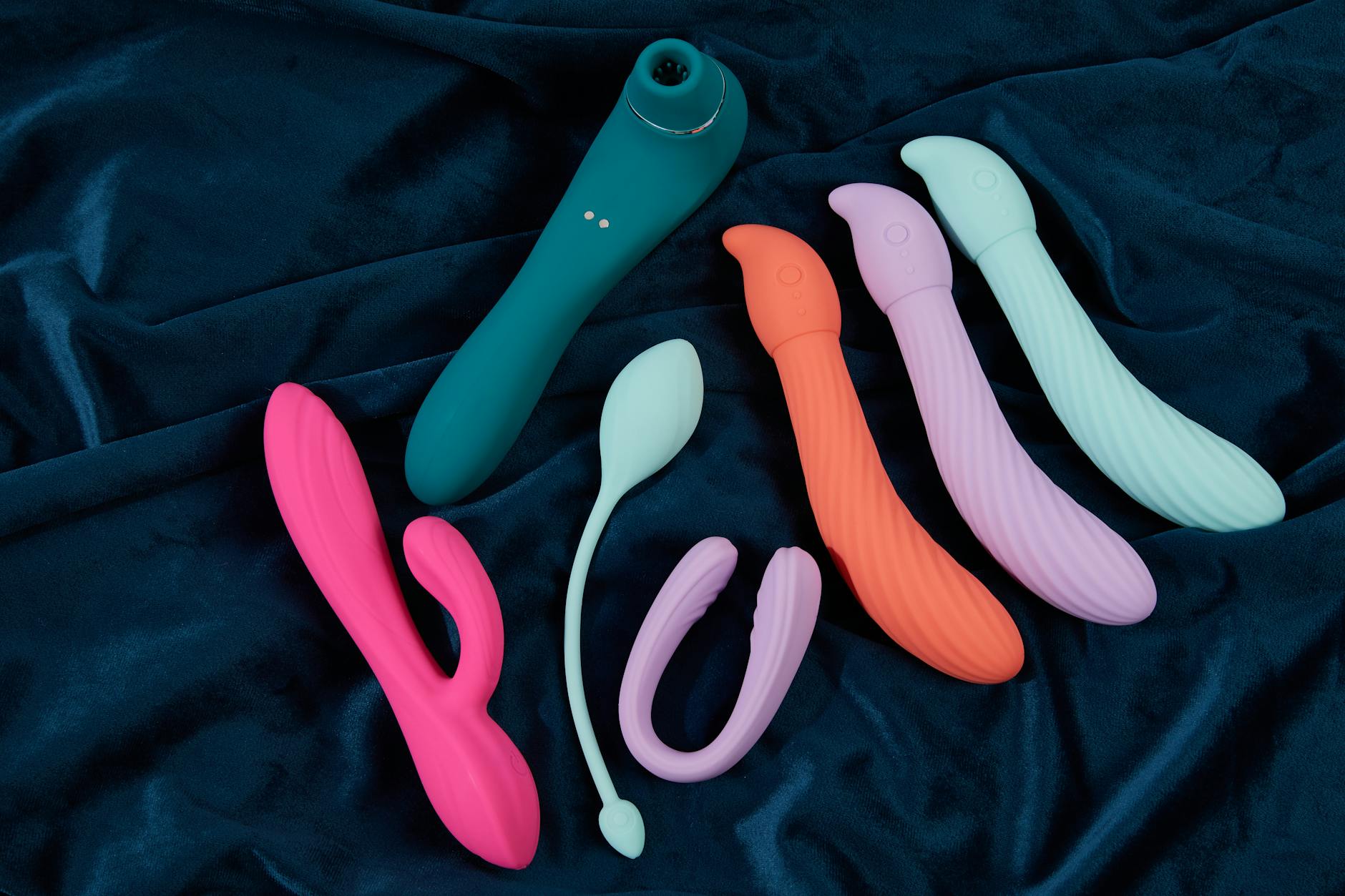 Woman thoughtfully holding blue and pink silicone vibrators, considering her options
