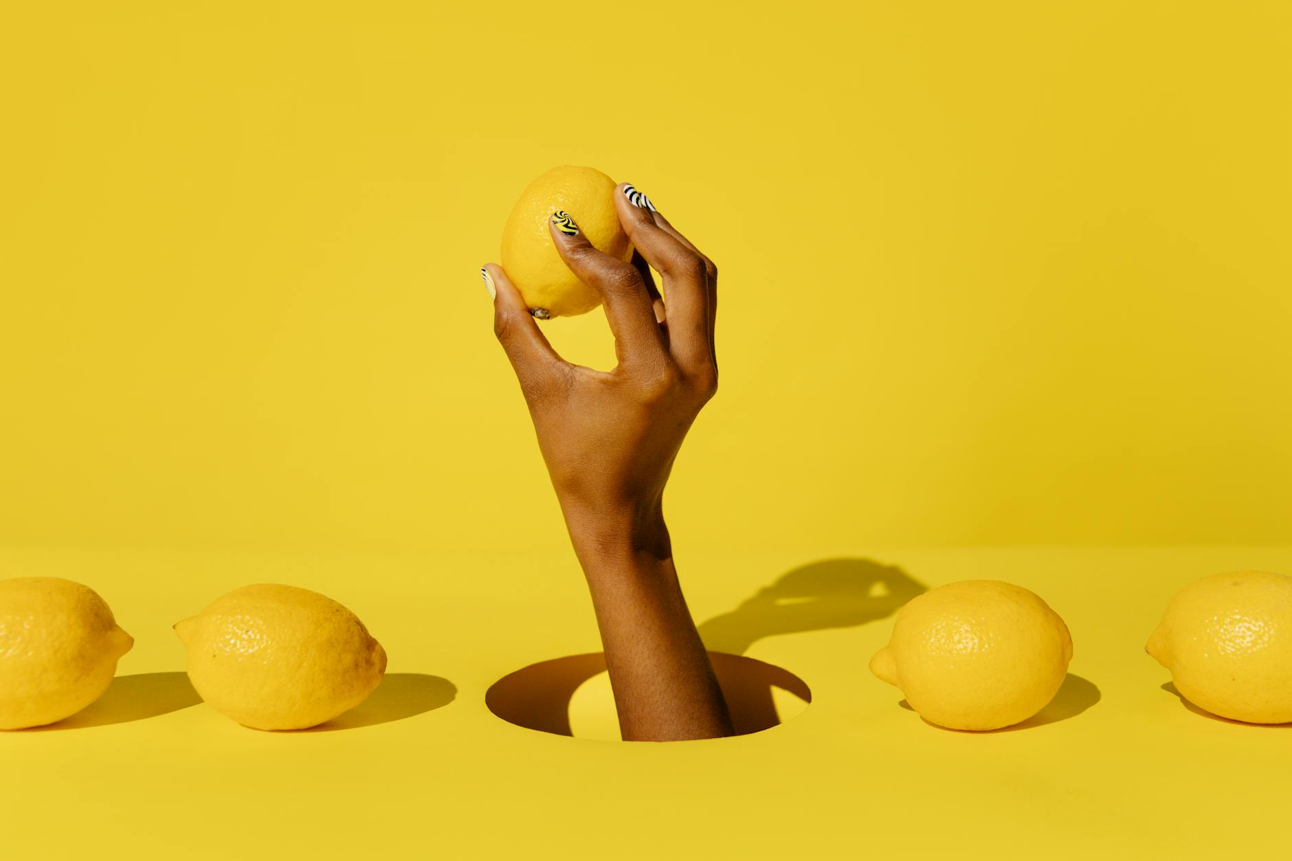 A hand holding a fresh lemon against a vibrant yellow background, symbolizing freshness and natural pleasure