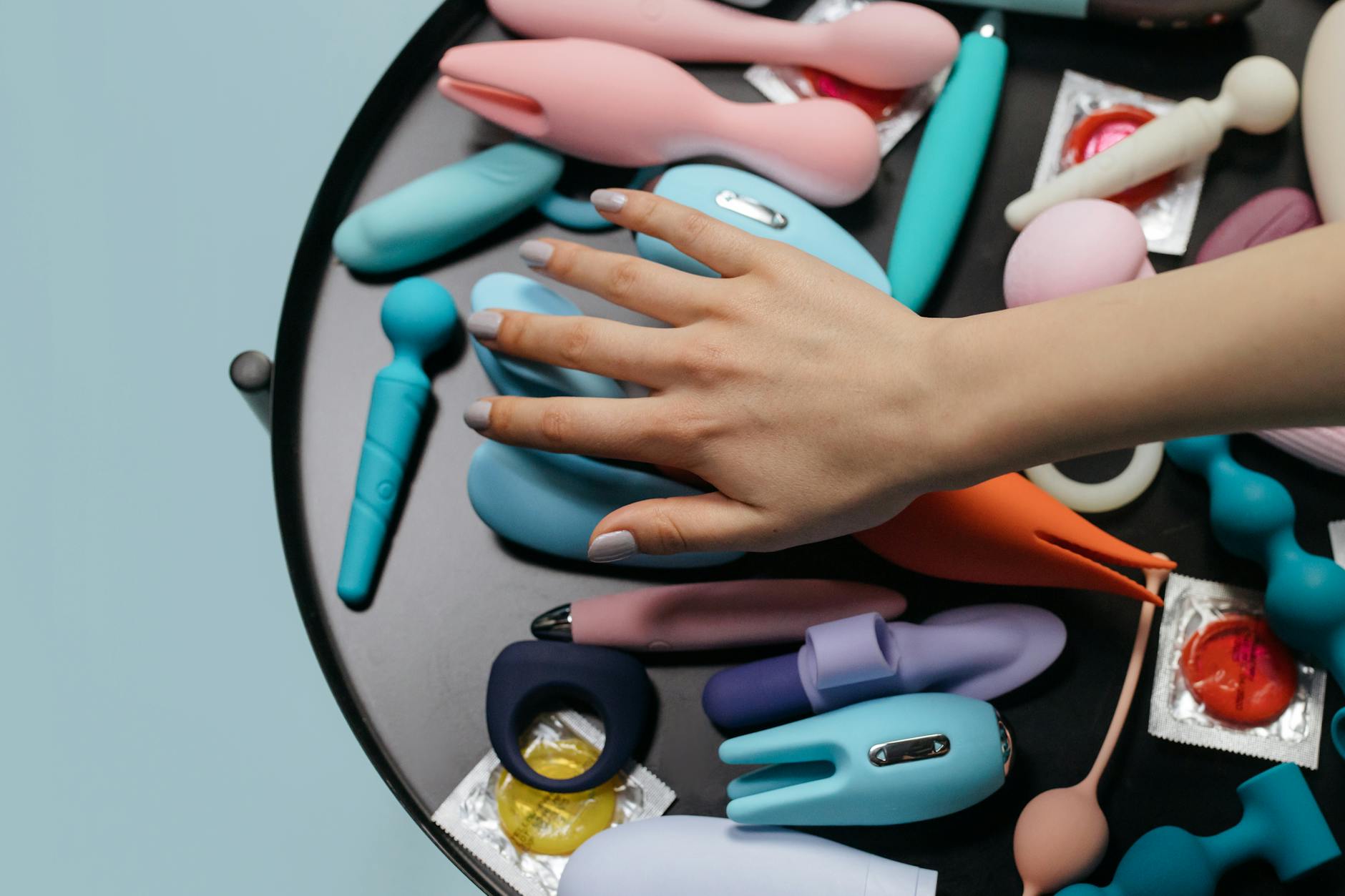 A hand reaching over a variety of colorful sex toys arranged on a table, representing reconnection tools for couples.