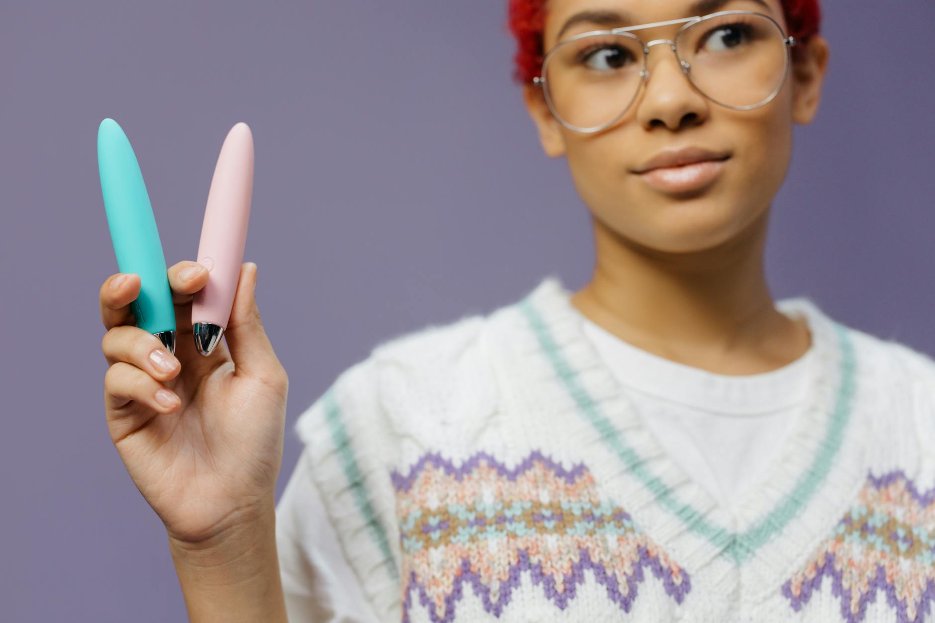 Woman holding two colorful vibrators against a purple background, representing choice and pleasure
