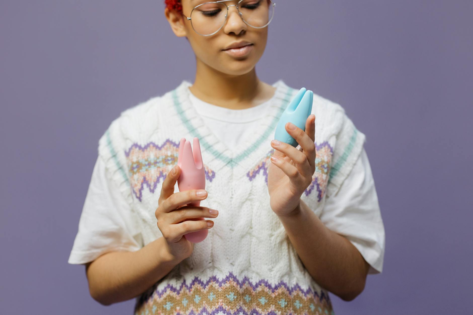 Woman holding blue and pink silicone vibrators in a contemplative, self-assured manner indoors.