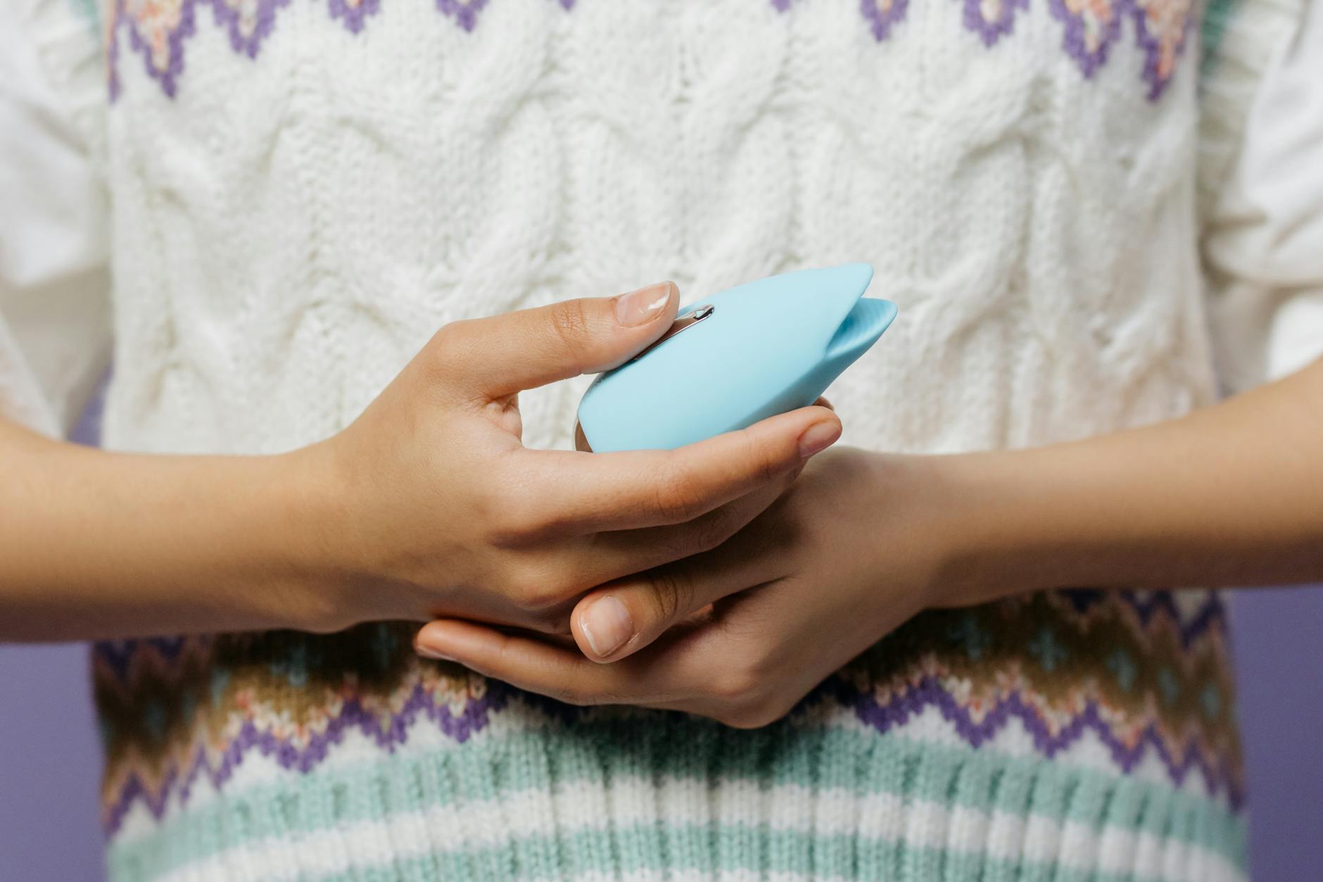 Two hands holding silicone vibrators together against a neutral background