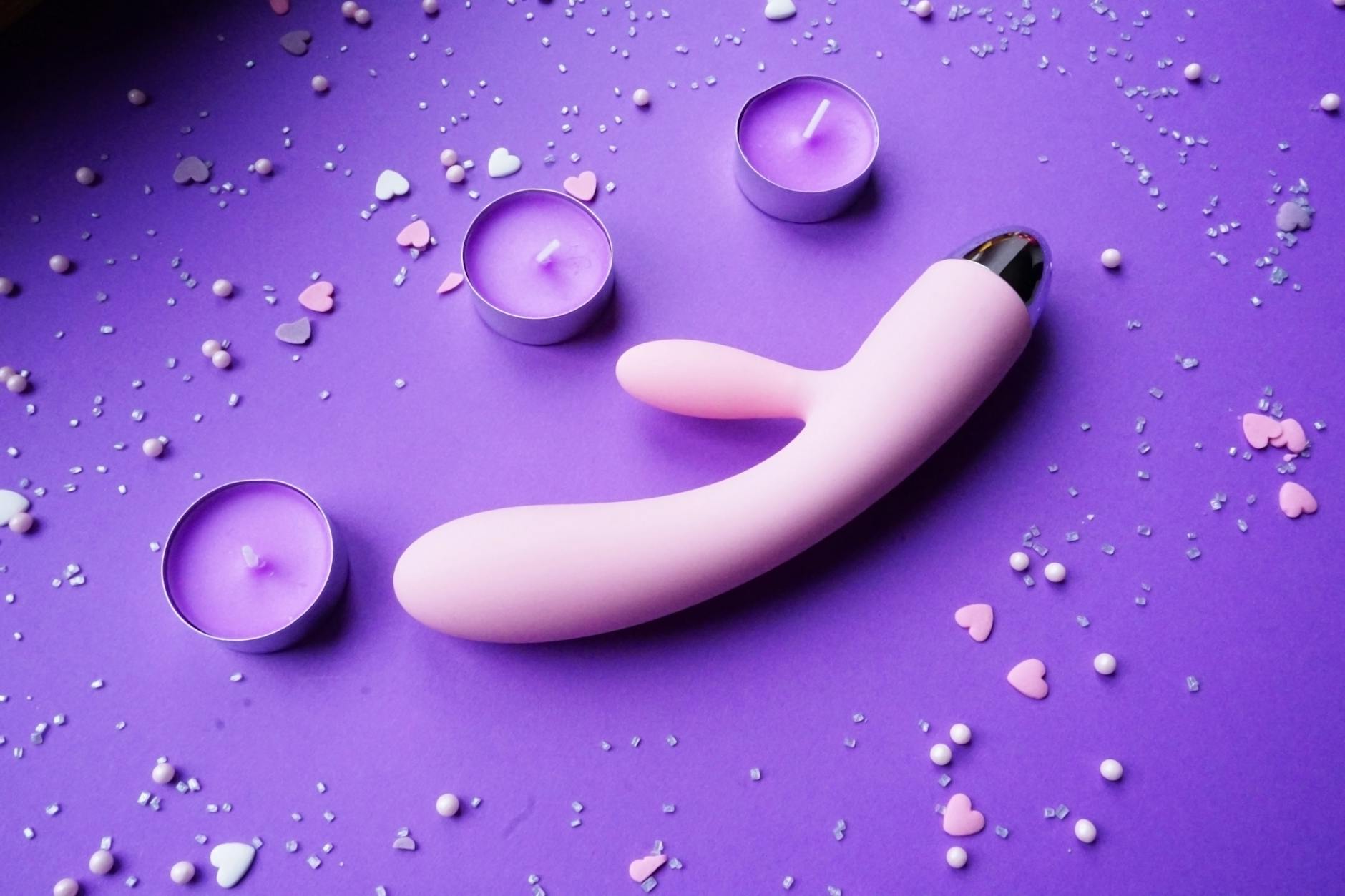 Pink vibrator on a soft background with candles and hearts, symbolizing safe, gentle pleasure